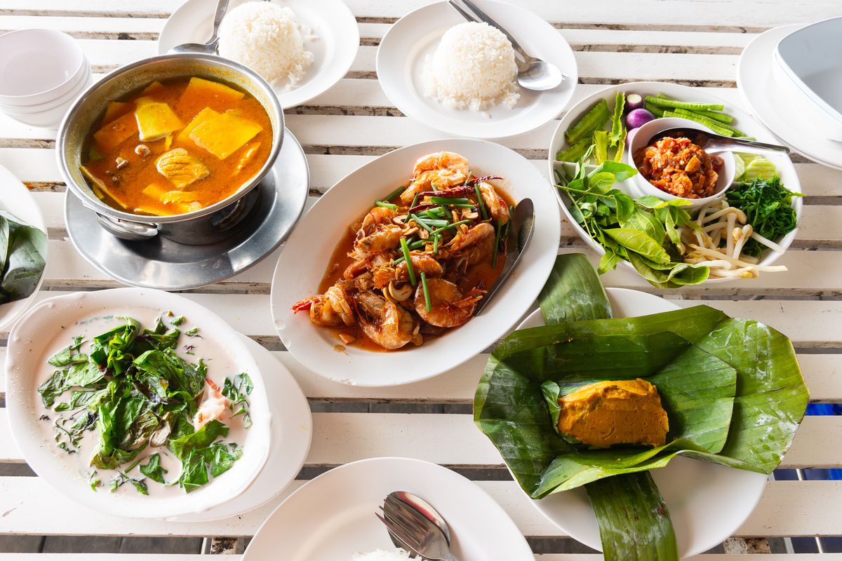 A mix of southern Thai and Phuket-style dishes on a white-slat table.
