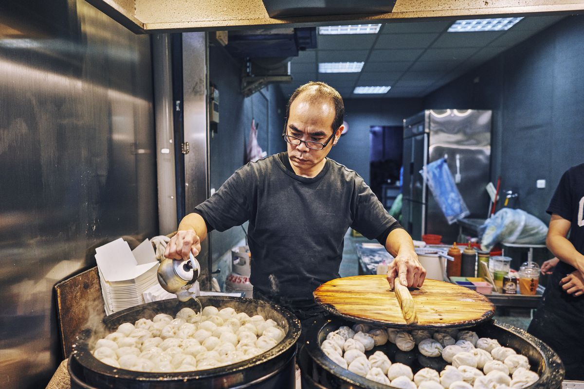 Man stands behind two large steamers filled with bao.