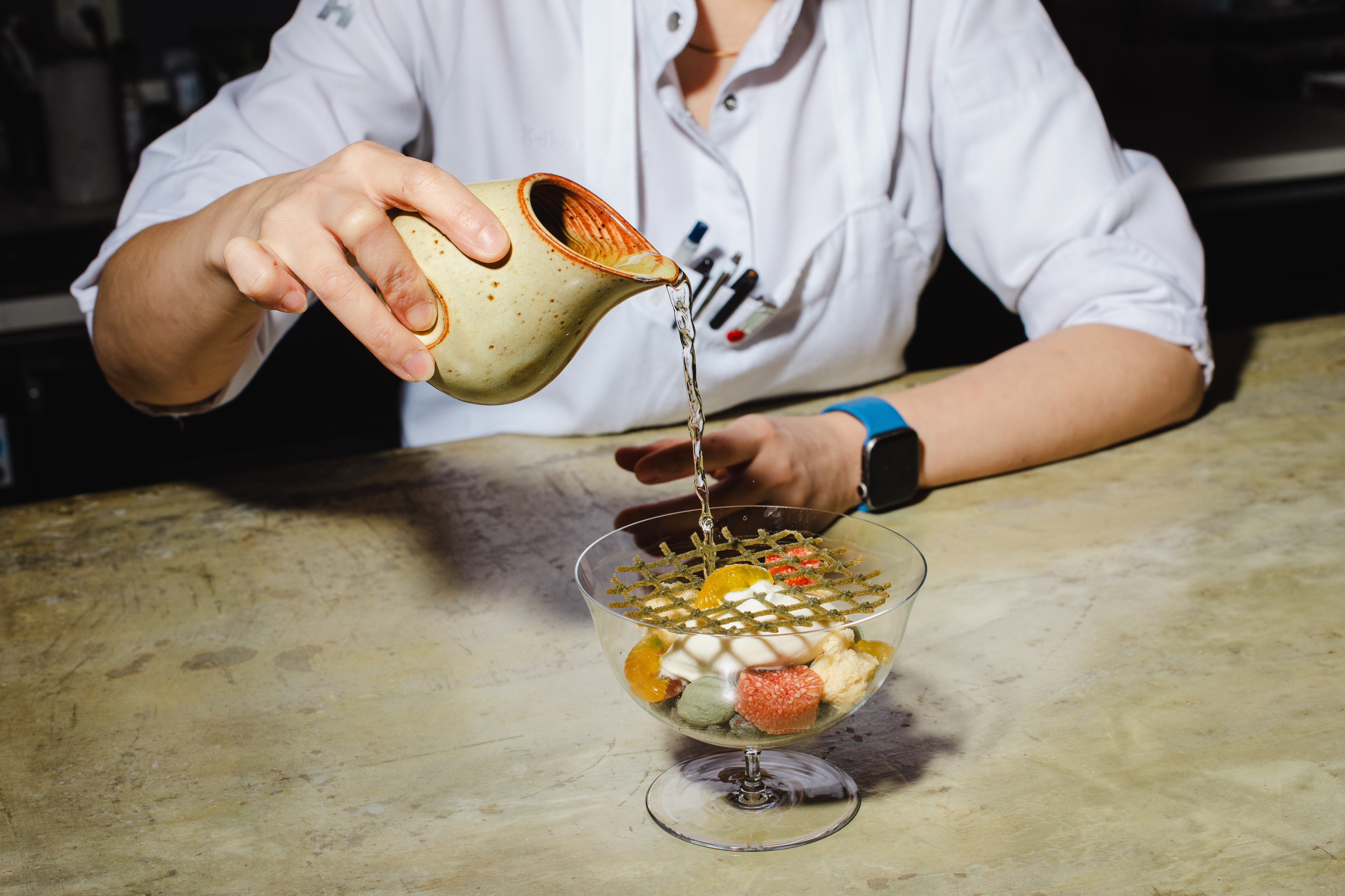 A person pours a pitcher into an elegantly arranged bowl of dessert