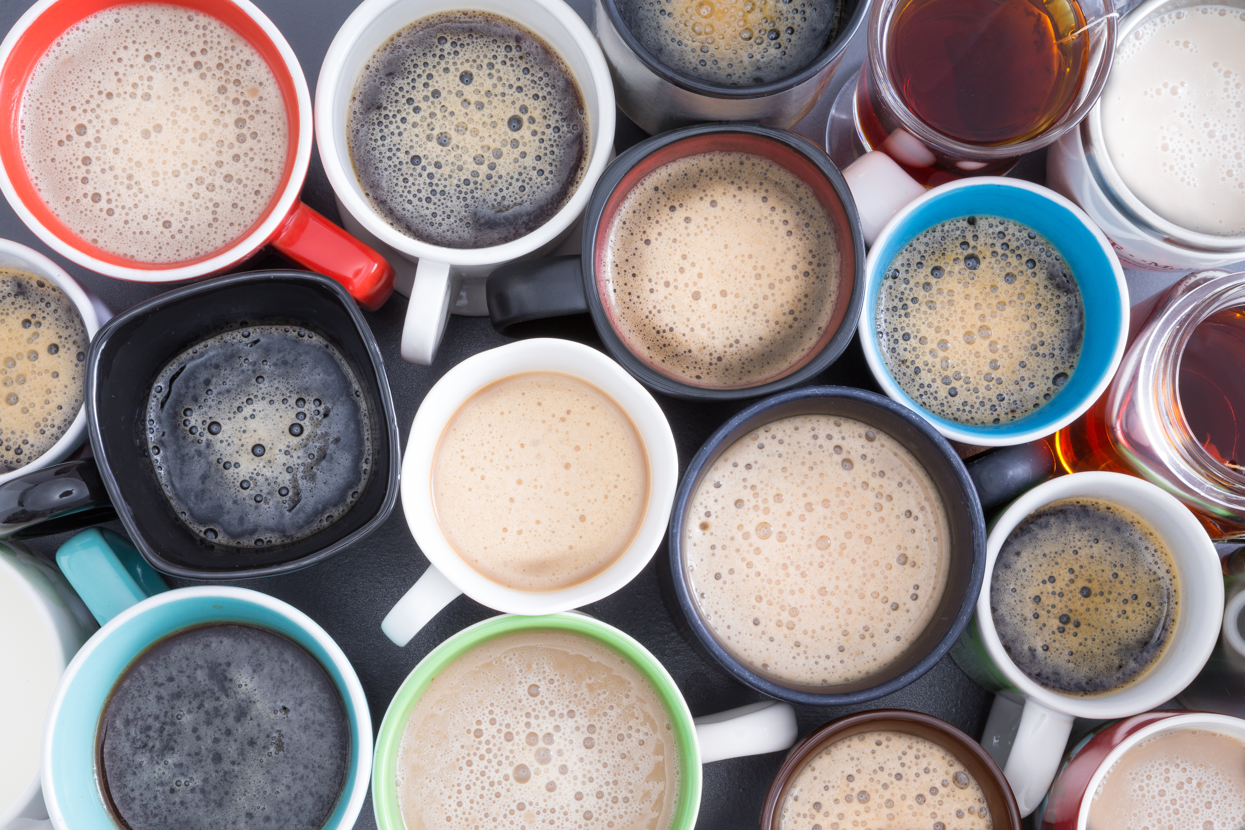 Dozens of cups and mugs filled with coffee, as seen from above.