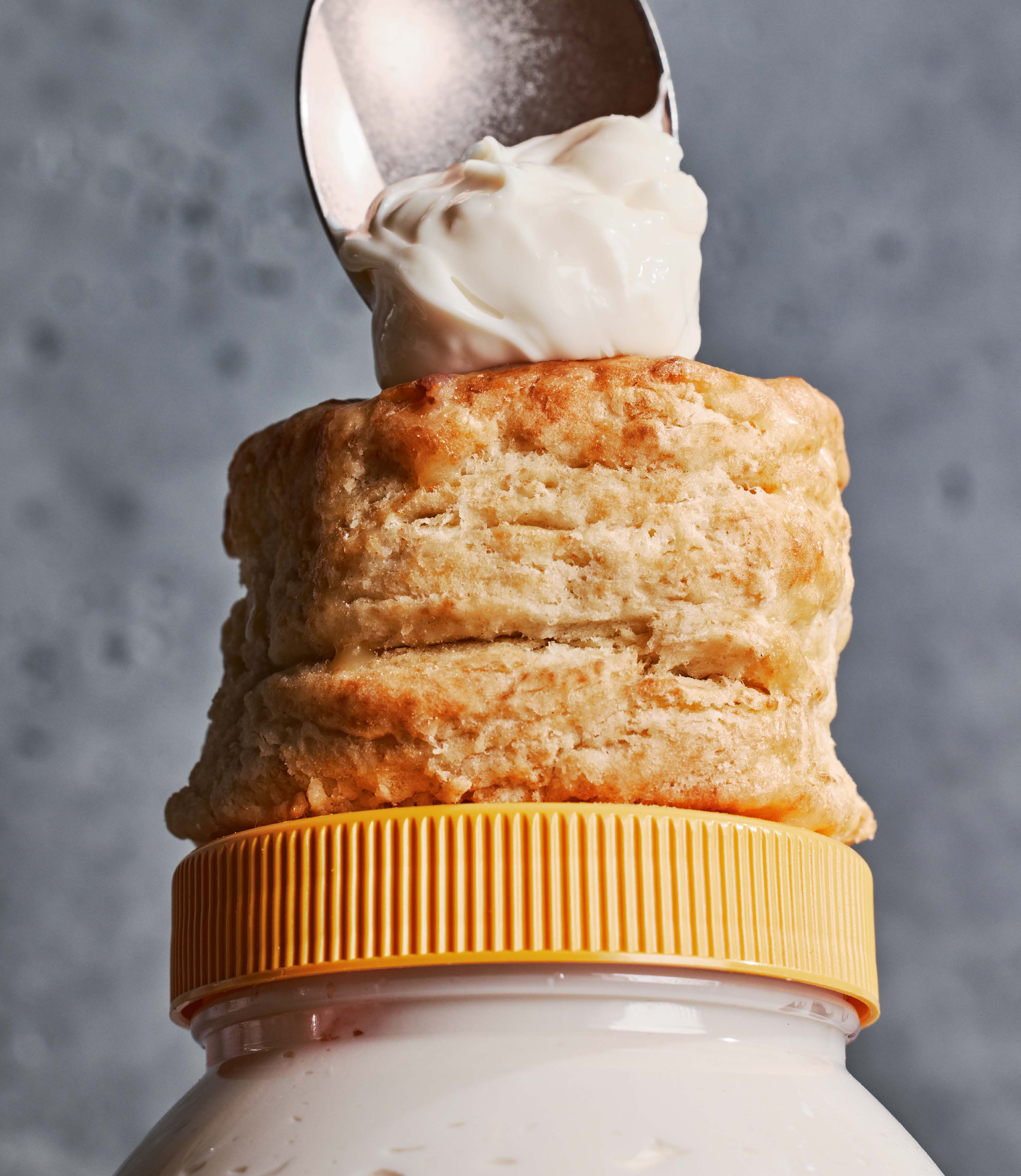 Mayonnaise is spooned onto a biscuit that sits on top of a jar of mayonnaise.