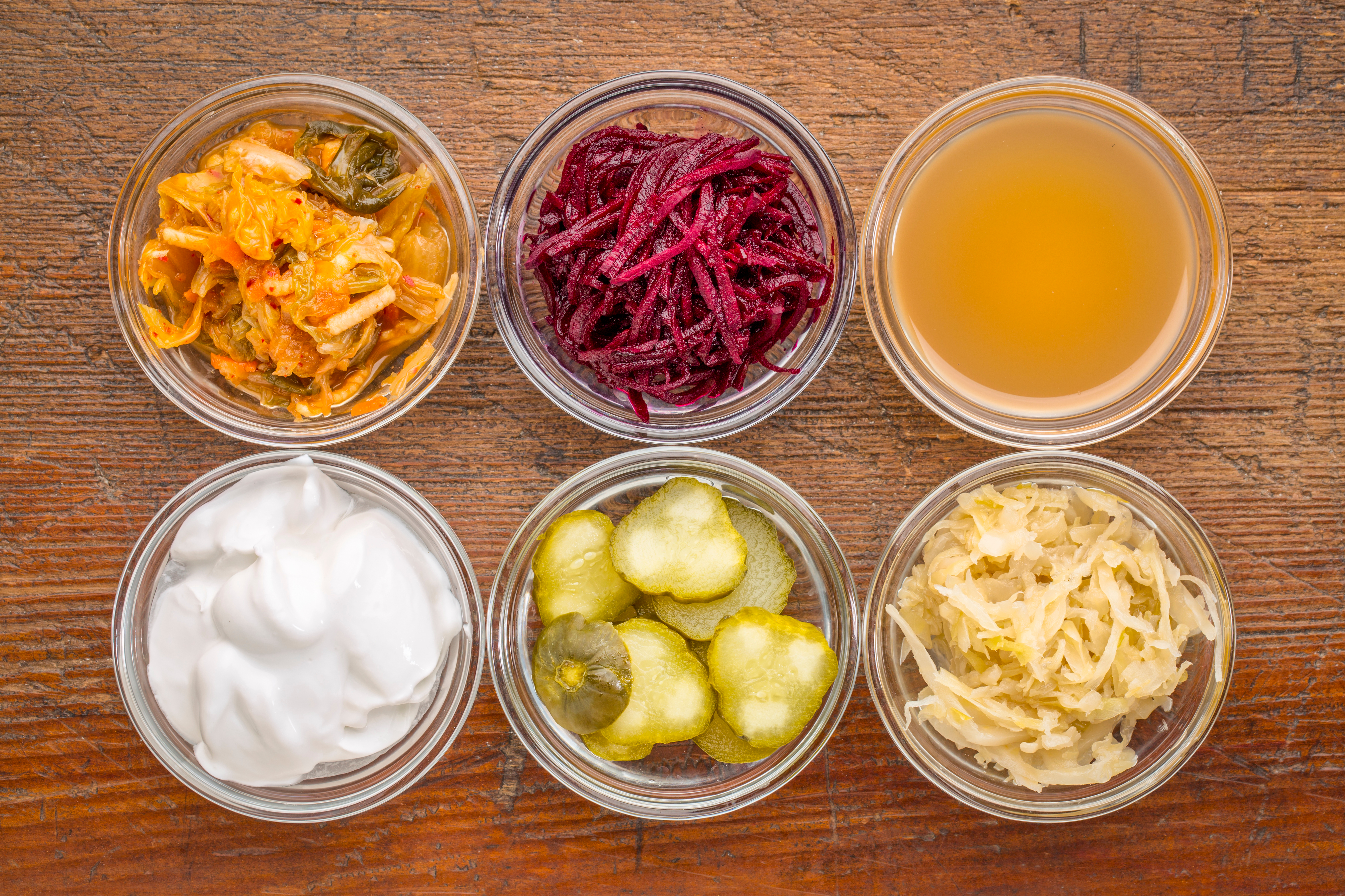 Six small ramekins containing: kimchi, shredded beets, broth, yogurt, pickles, and sauerkraut.