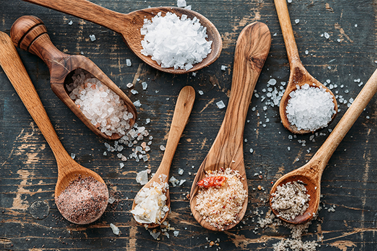 Different sized wooden spoons featuring different types of salt in varying crystal sizes.