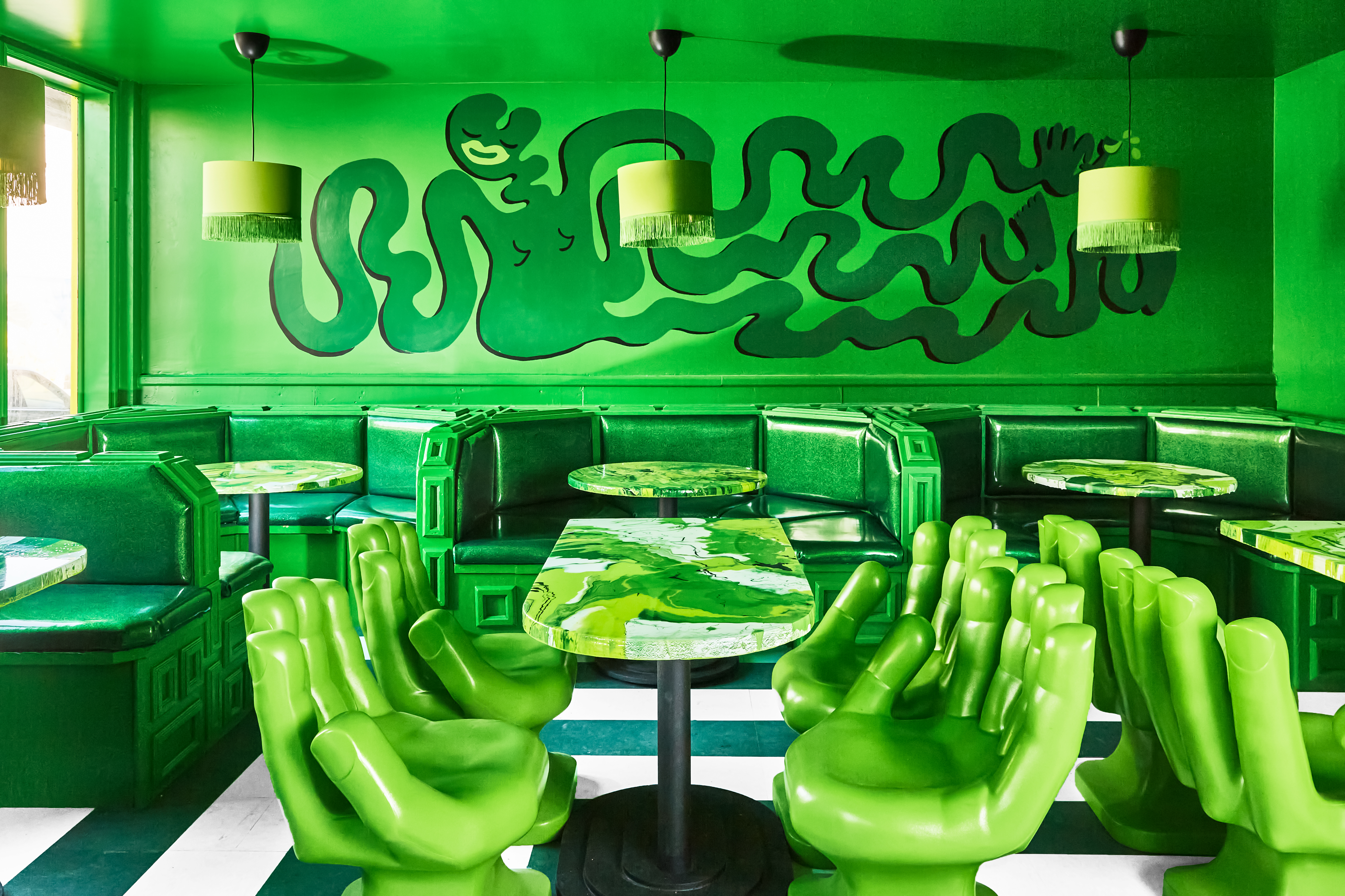 Bright green walls, green hand-shaped chairs, and green booths make up a boldly monochrome dining room.