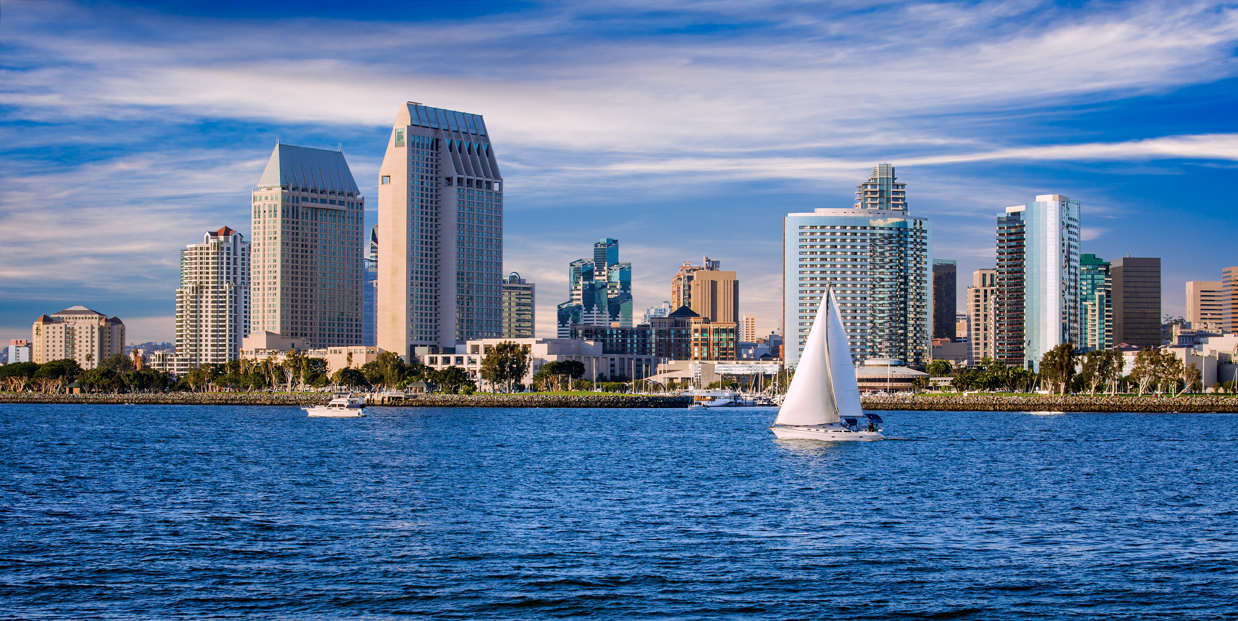 A sailboat in water in from of the buildings that make up the downtown San Diego skyline.
