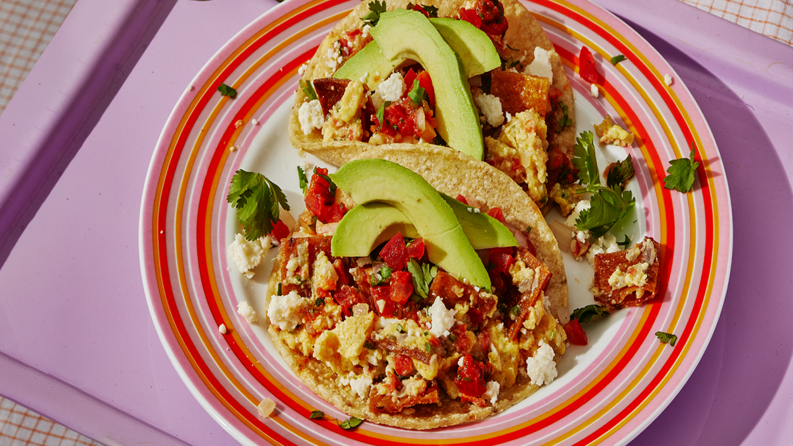 A plate with two migas tacos topped with sliced avocado.